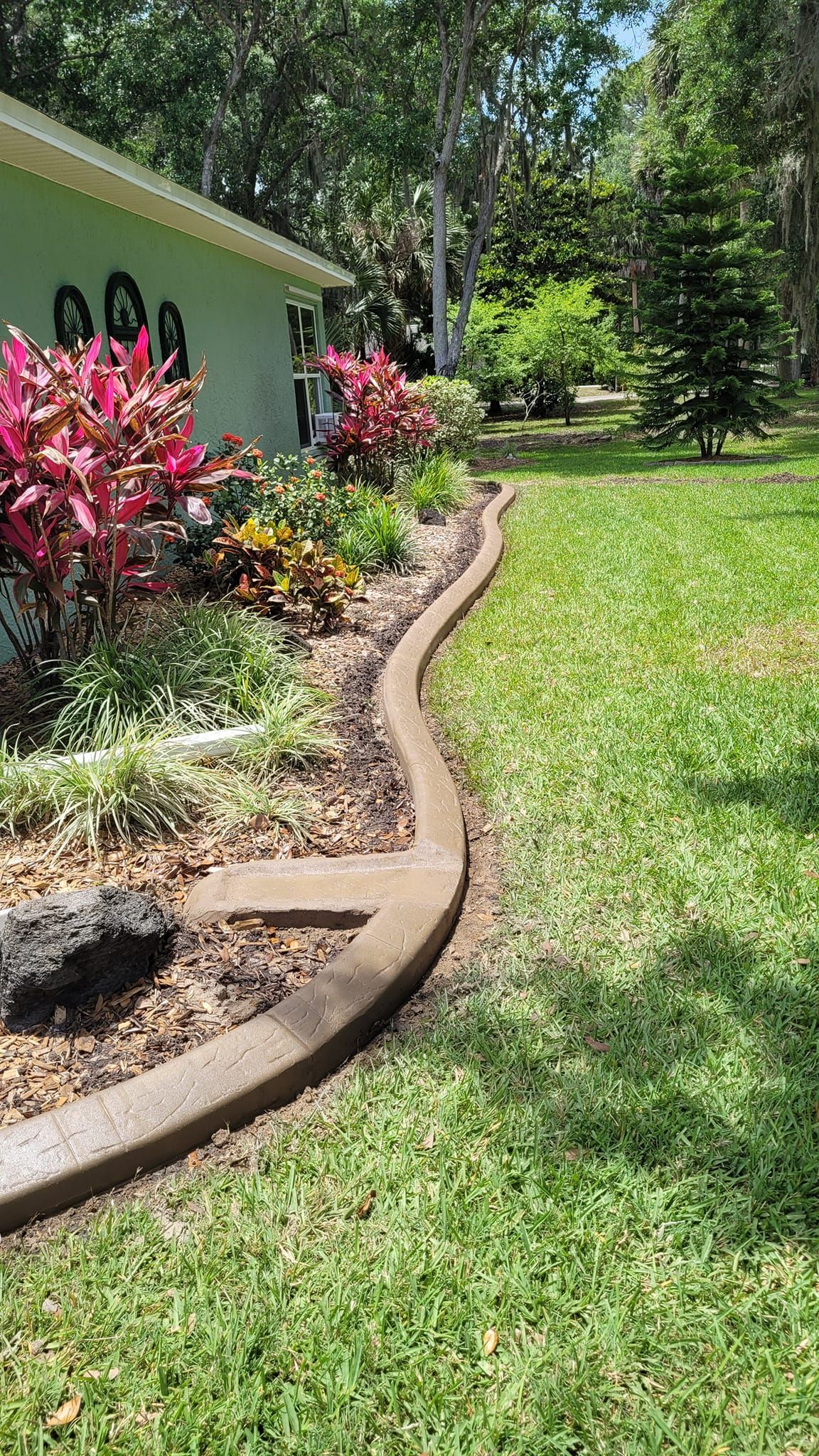 There is a concrete curb in the middle of a lush green lawn.
