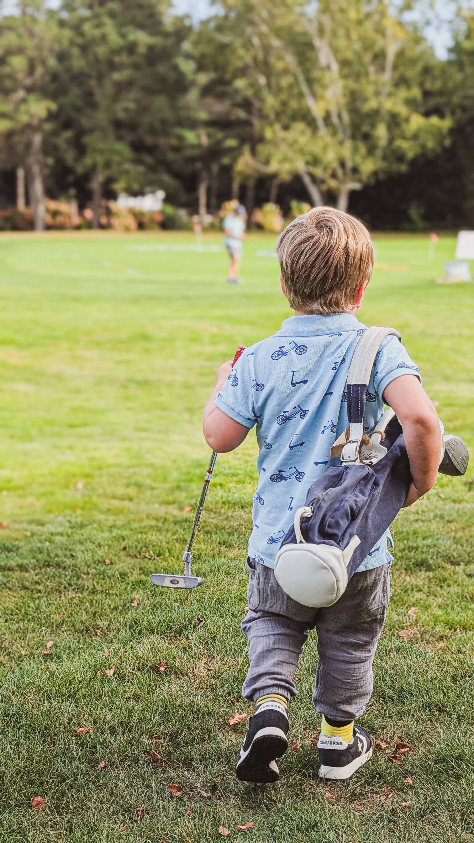 A man and two boys are walking down a path carrying golf bags.