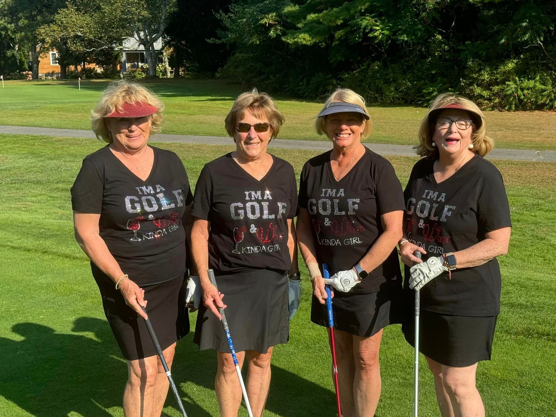 Four women are standing on a golf course holding golf clubs.