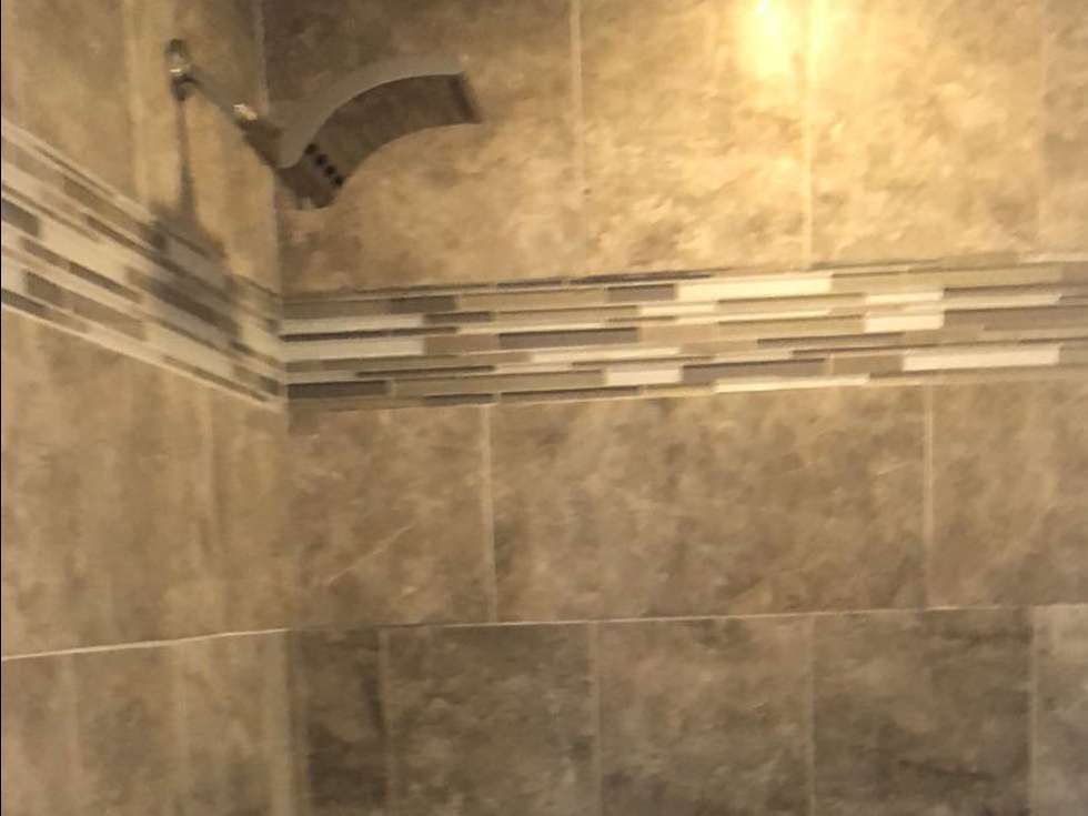 A modern shower interior featuring large beige tiles, a horizontal mosaic accent strip, and a mounted rainfall showerhead.
