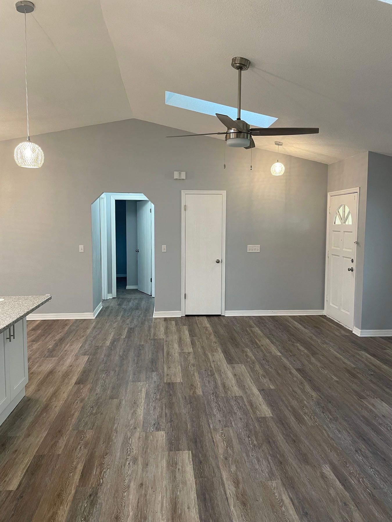 A room with gray walls, wood-look flooring, a white door, a ceiling fan, a pendant light, and an open doorway.