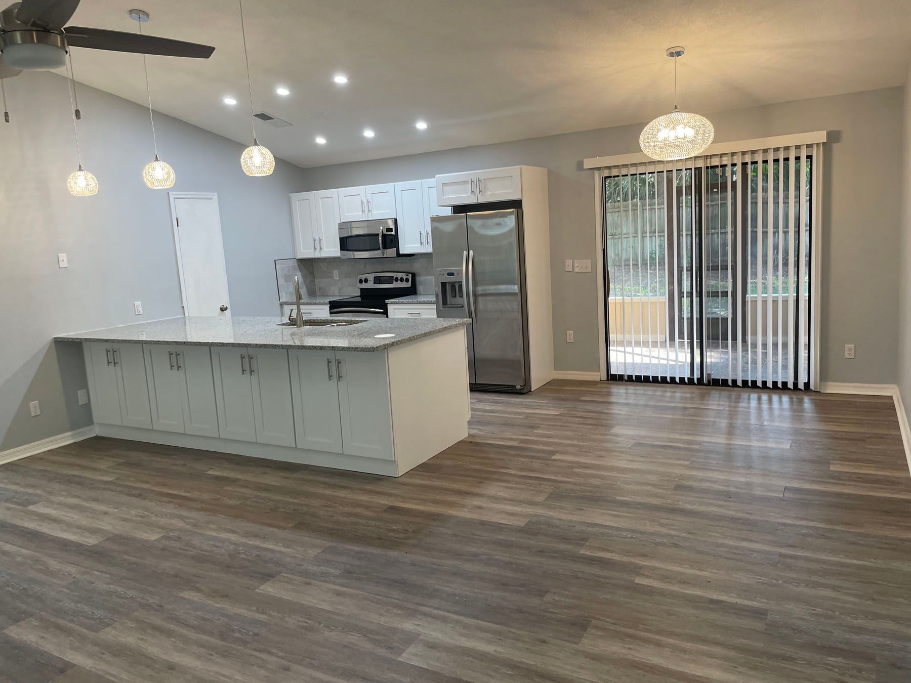 An open kitchen with white cabinets, a large island, stainless steel appliances, and wood-look flooring.