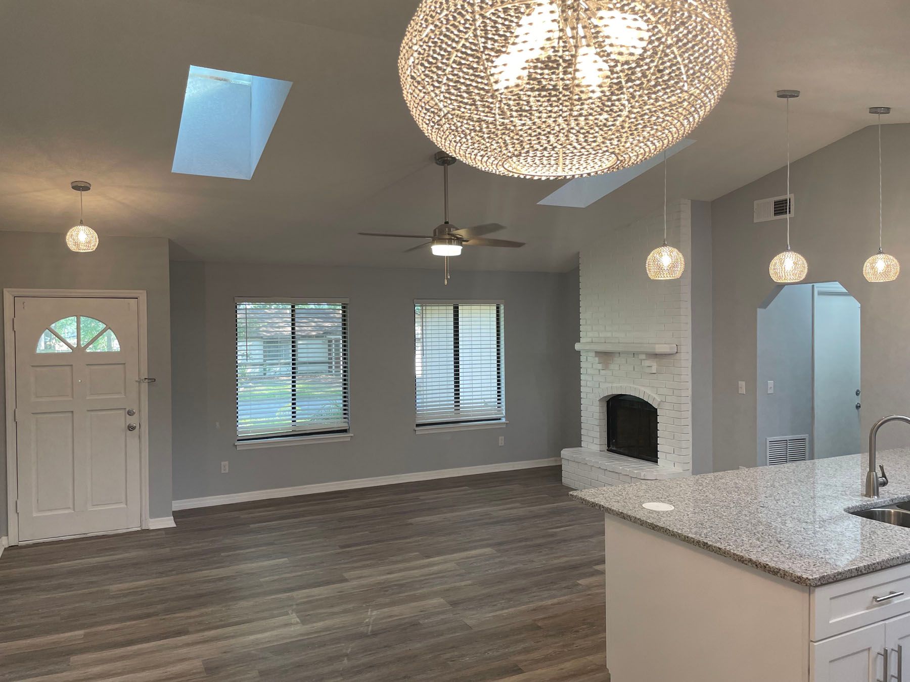 An open-concept living area with grey walls, hardwood-style floors, a stone fireplace, skylights, and a granite island.