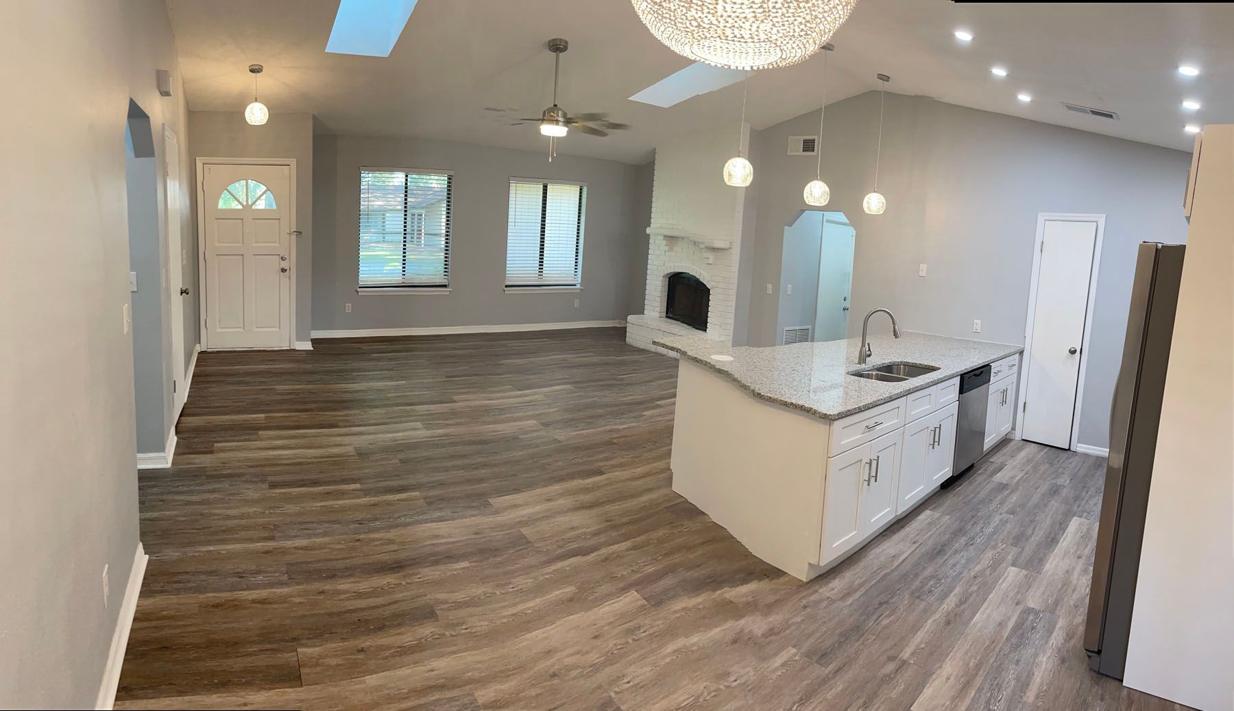 A panoramic shot of an open-plan living area with gray walls, wood-look flooring, a kitchen island, and a fireplace.