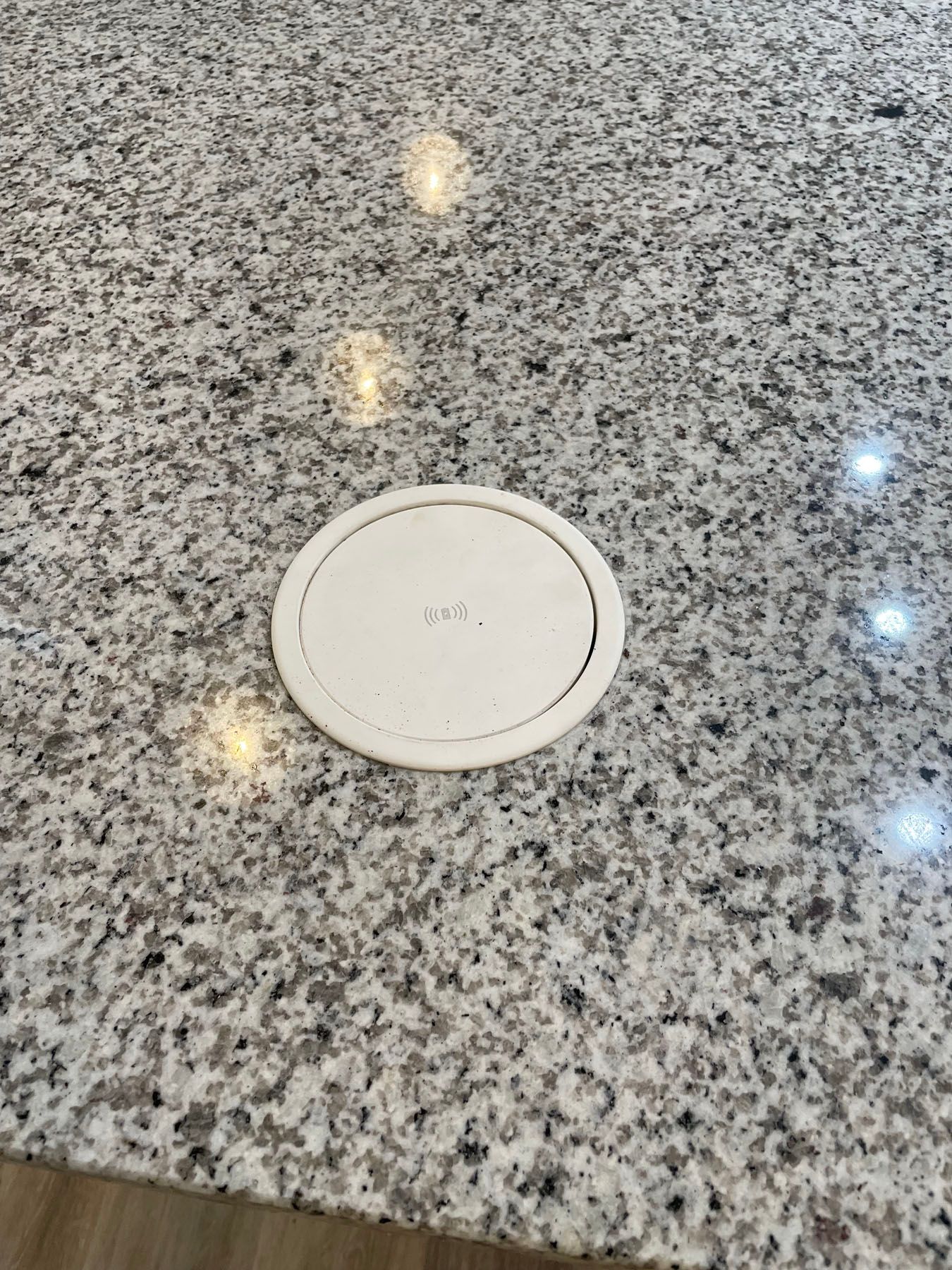 A white, circular pop-up electrical outlet installed flush into a speckled granite countertop.
