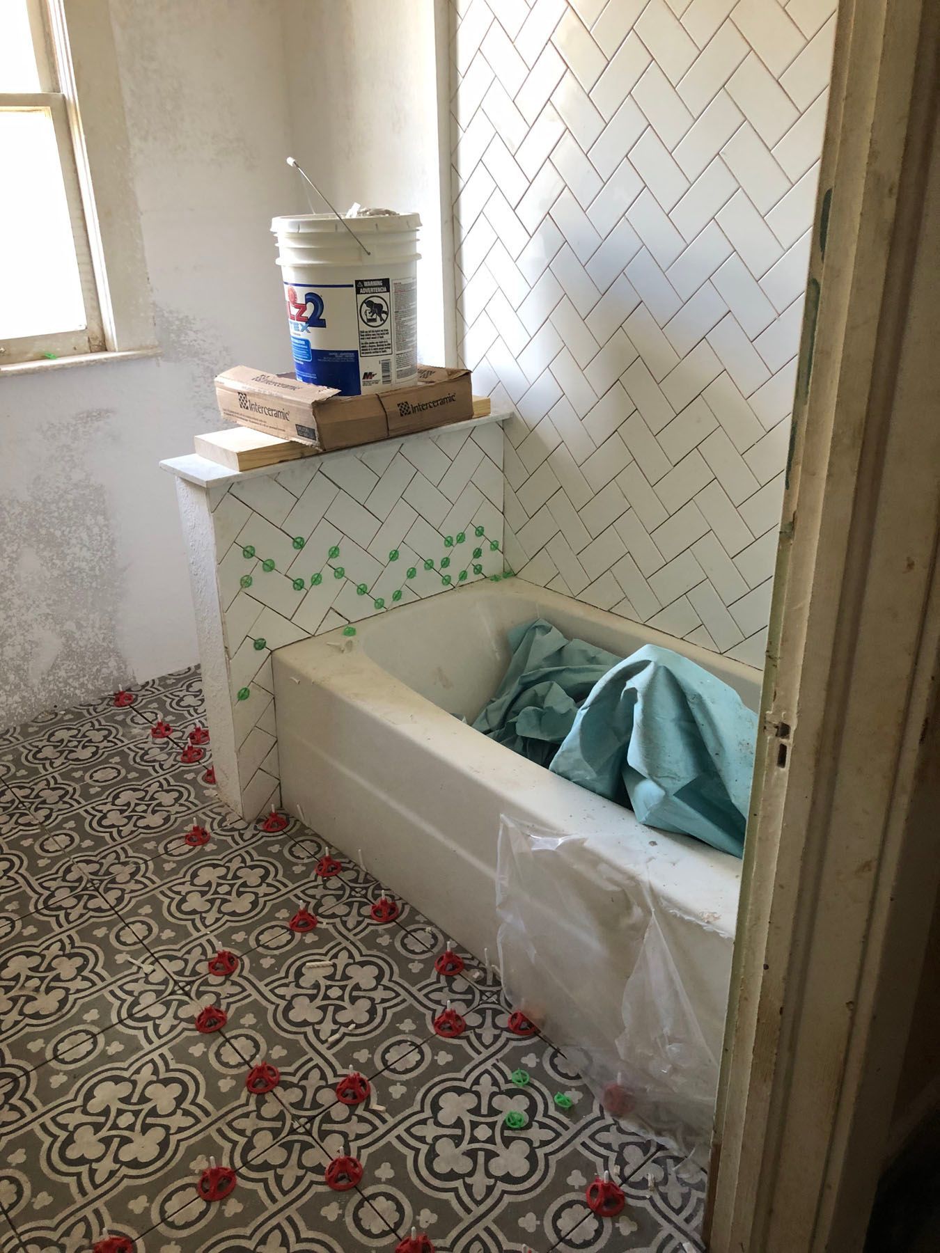 Bathroom under renovation with white herringbone tiled walls, patterned gray floor tiles, and a bathtub covered in a cloth.