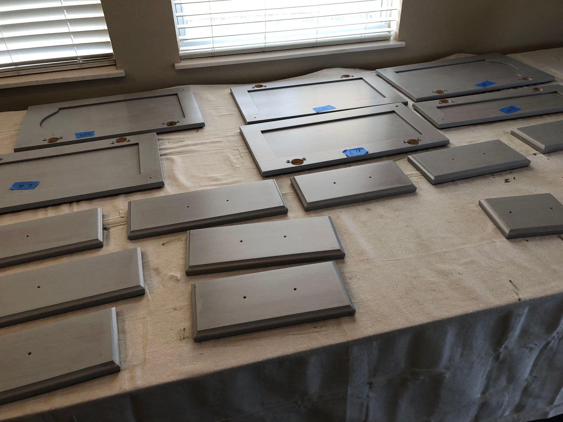 Light gray kitchen cabinet doors and drawer fronts laid out on a cloth-covered table to dry after being painted.