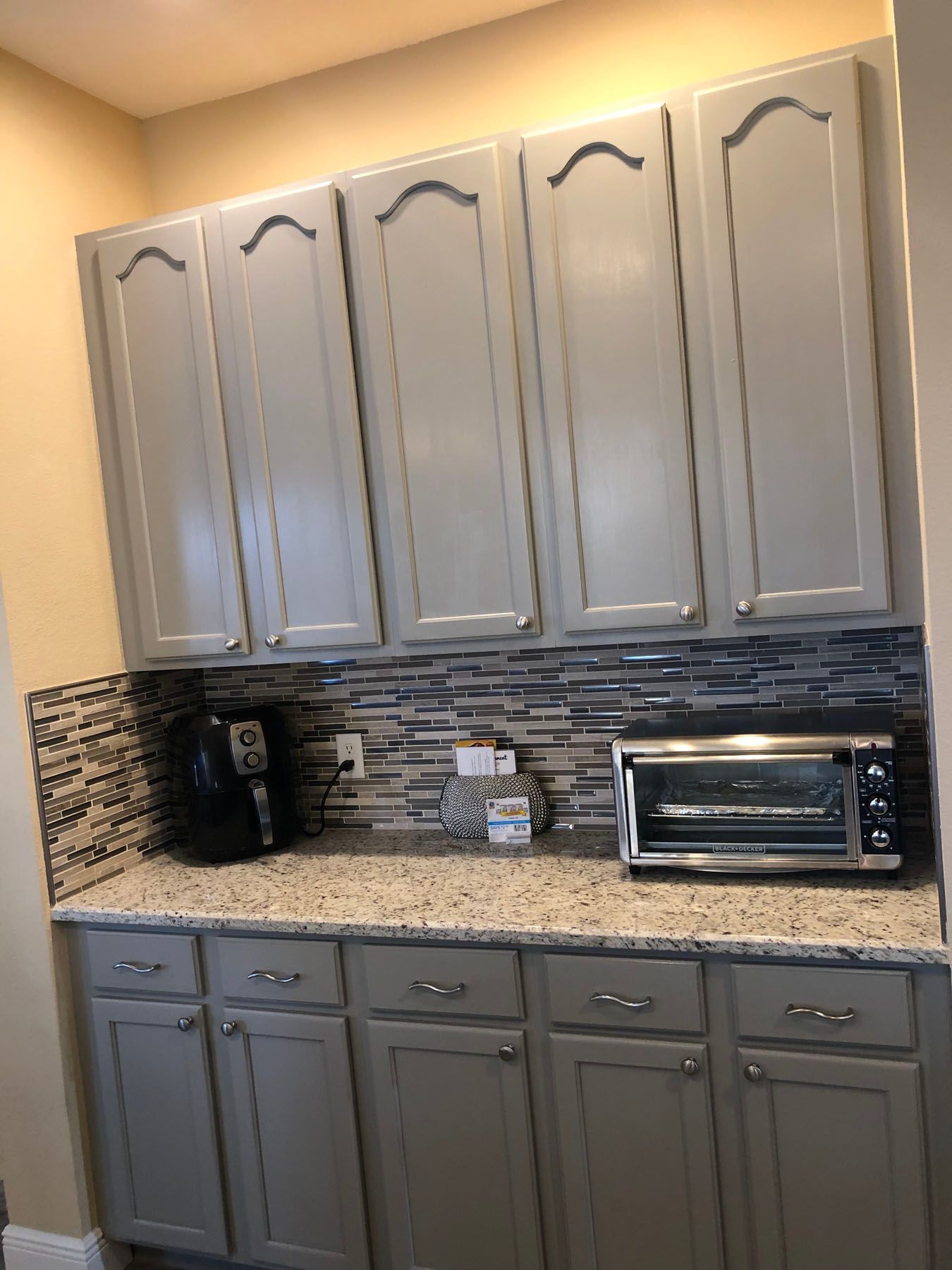 A kitchen counter area with gray cabinets, a speckled granite countertop, and a decorative tile backsplash.