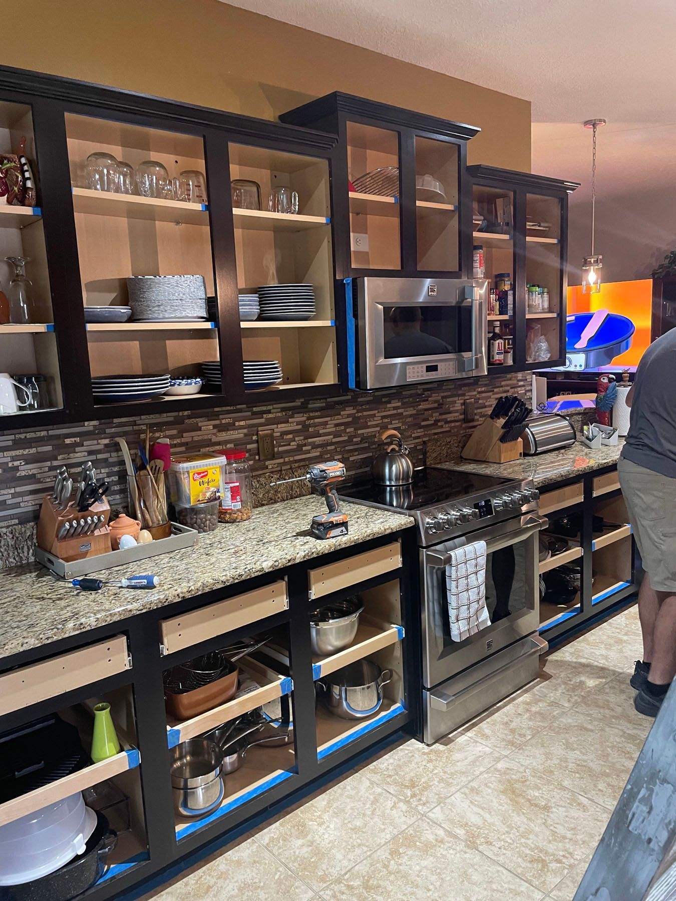 A kitchen in progress with dark cabinets installed above and below a granite countertop, with doors yet to be attached.