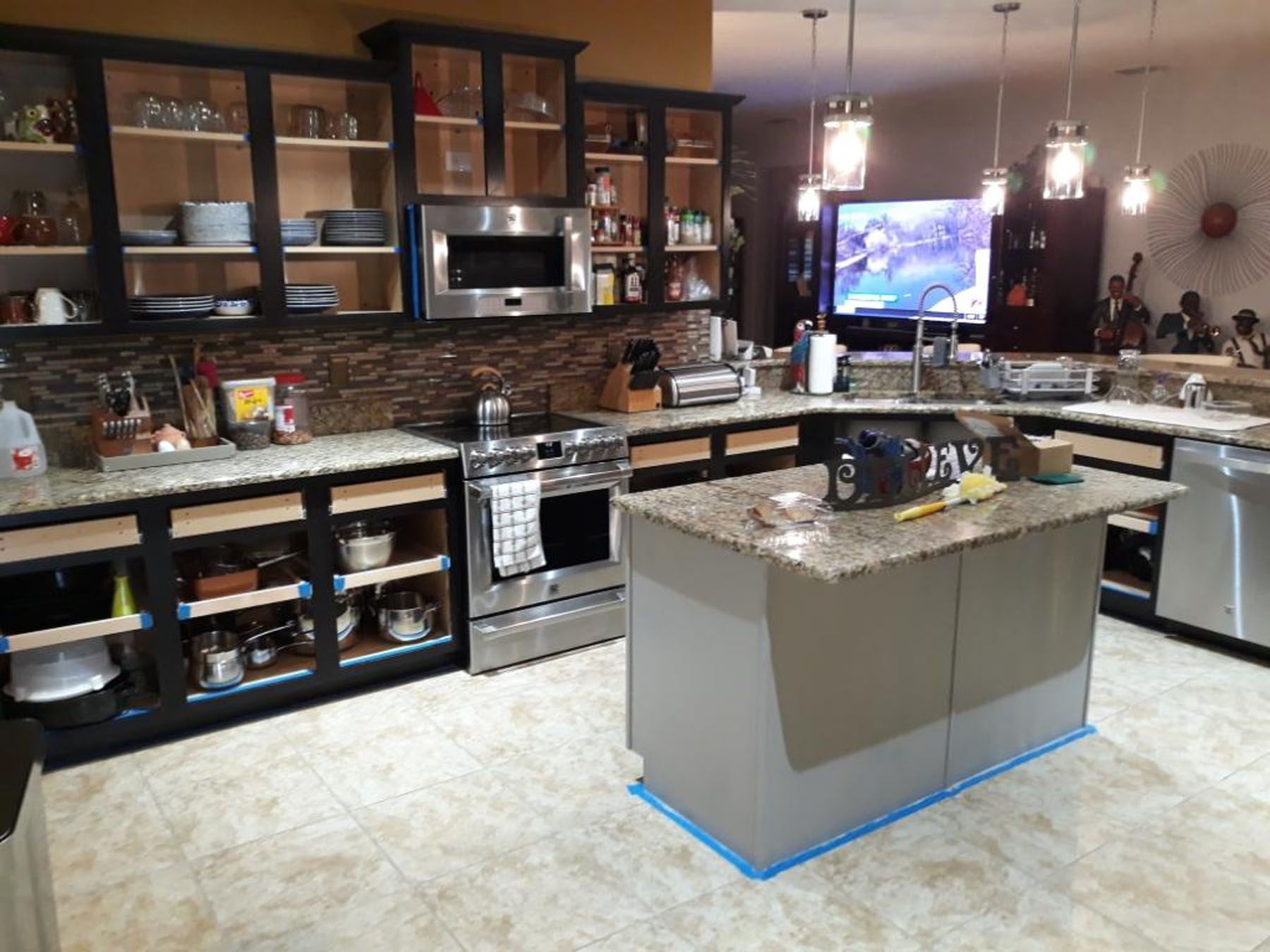 A kitchen renovation in progress, featuring dark cabinets with missing drawer fronts, a granite island, and stainless steel.