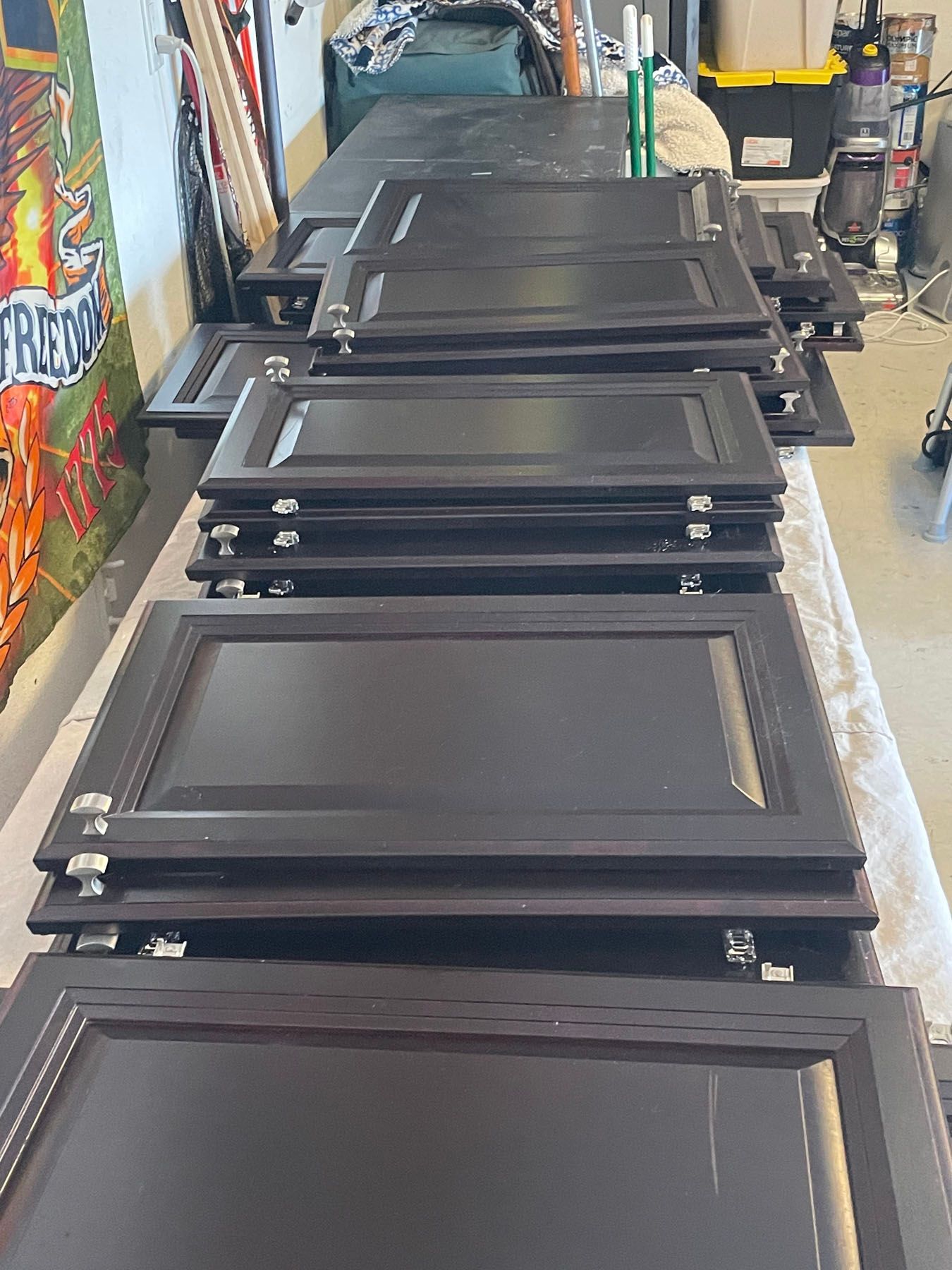 Multiple dark brown cabinet doors stacked in rows on a table in a workshop setting.