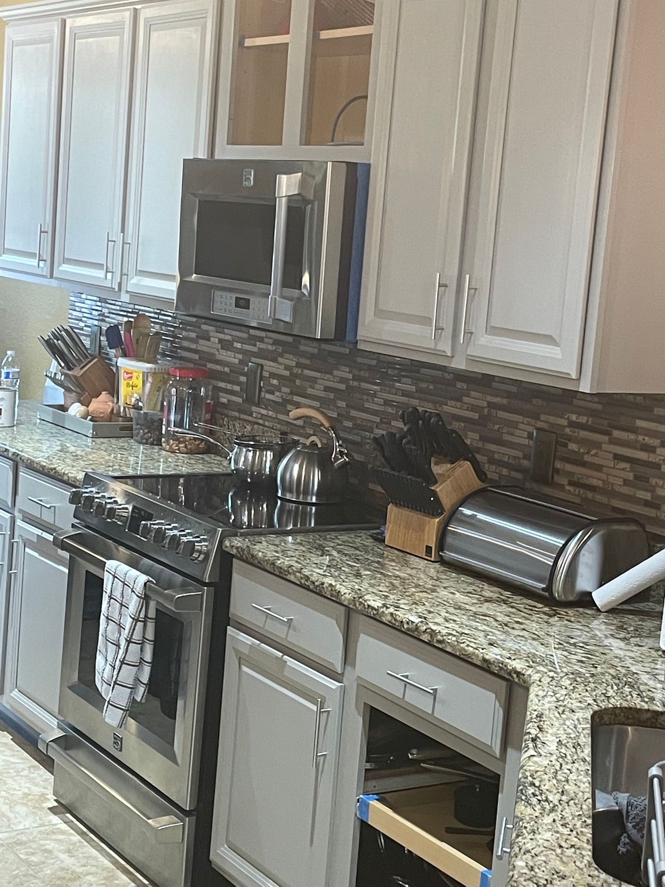 Kitchen with white cabinets, stainless steel appliances, granite countertops, and a brown tiled backsplash.