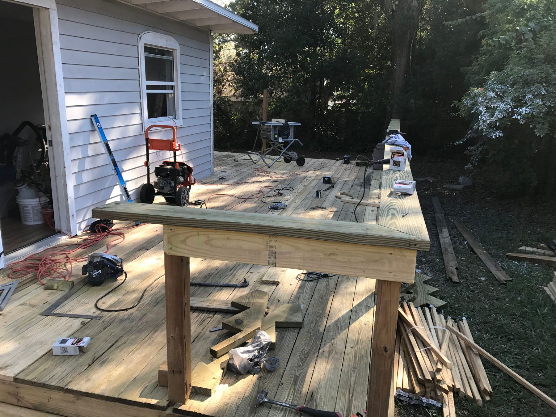 A wooden deck under construction with a support frame in the foreground, adjacent to a light gray house.