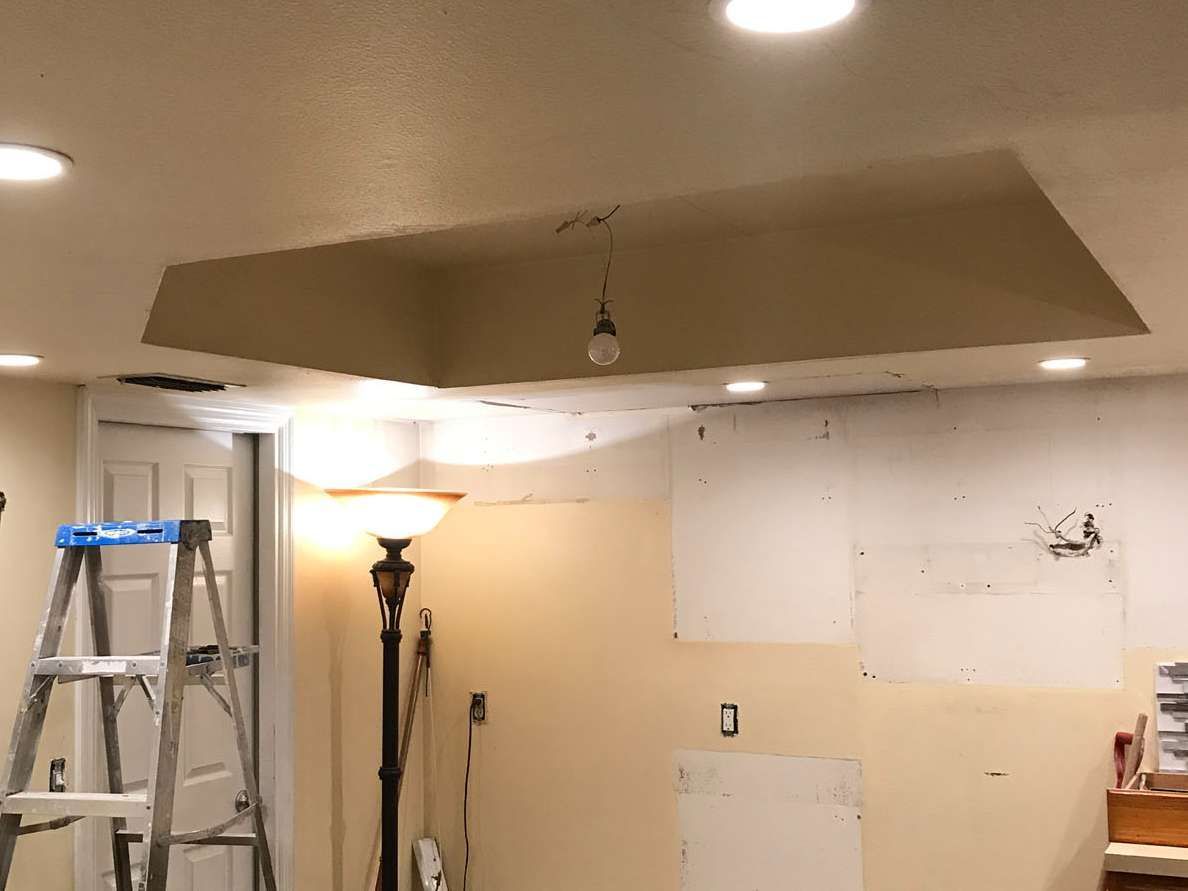 A room under renovation with a ladder, a floor lamp, and a tray ceiling with a single dangling light bulb.