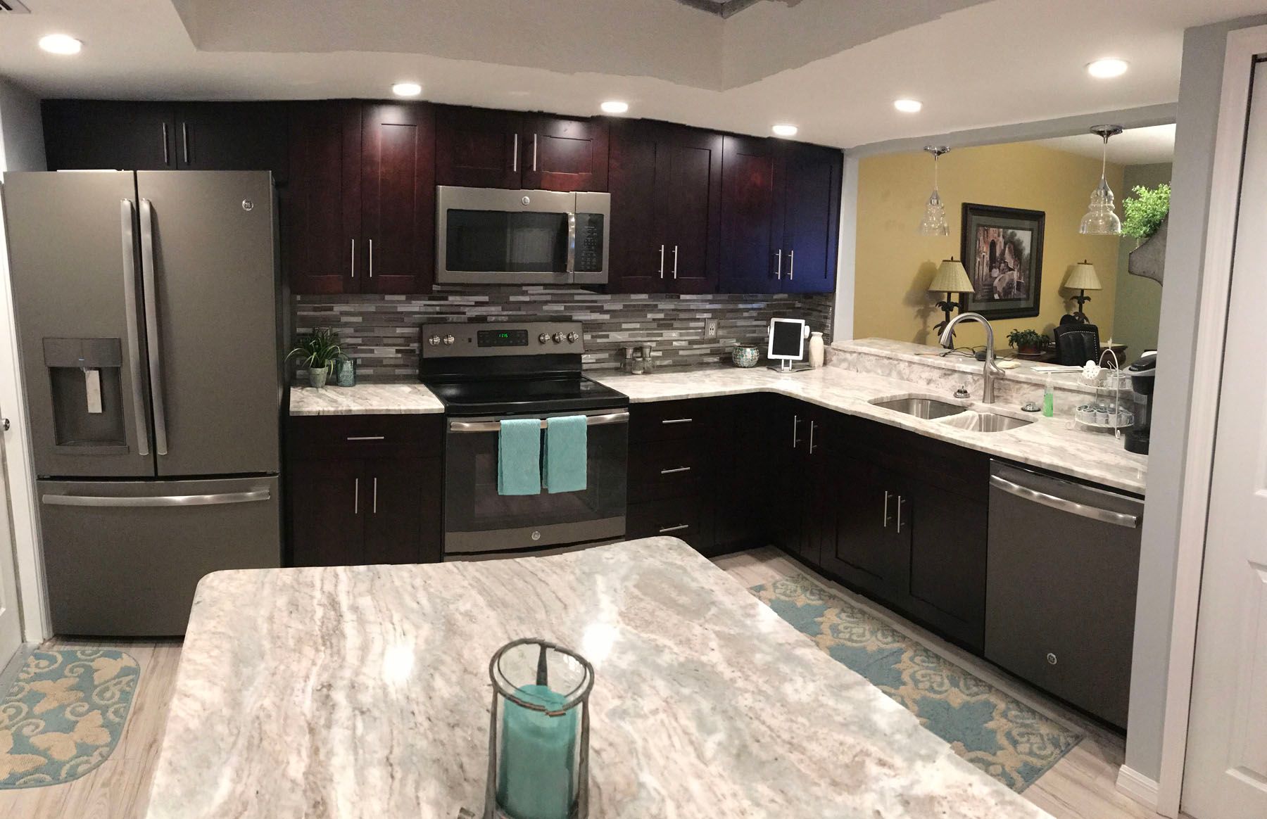 A modern kitchen with dark brown cabinets, grey granite countertops, stainless steel appliances, and an island.