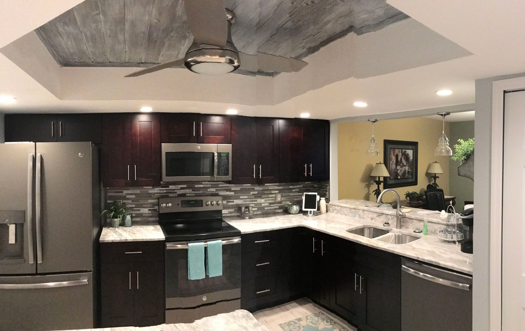 A modern kitchen with dark cabinetry, stainless steel appliances, marble-look countertops, and a textured tray ceiling.
