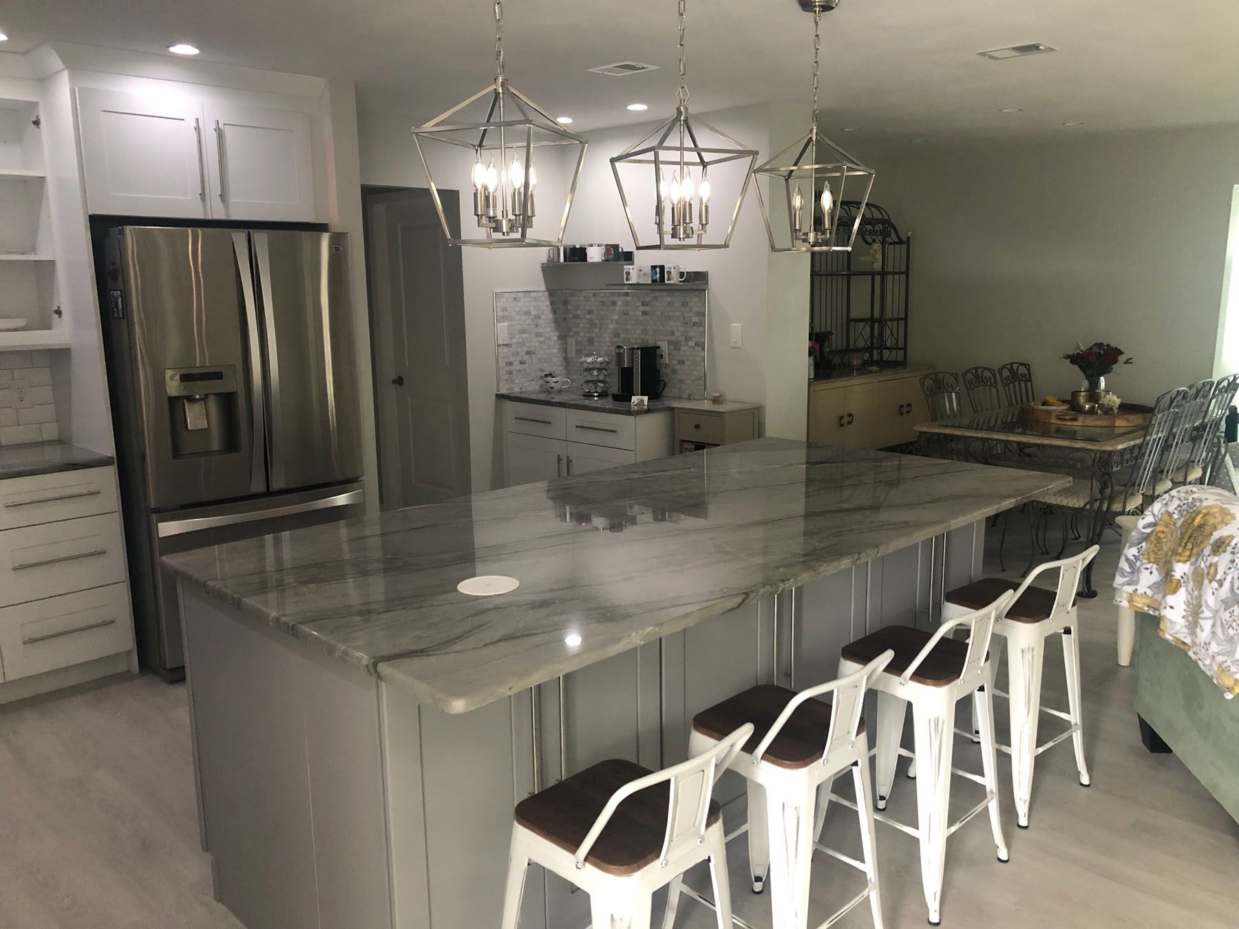 A modern kitchen features a large grey island with a marble countertop, three white barstools, and three pendant lights.