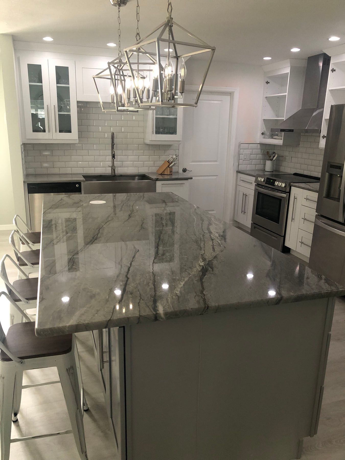 Modern kitchen with a large grey granite island, white cabinets, stainless steel appliances, and geometric pendant lights.