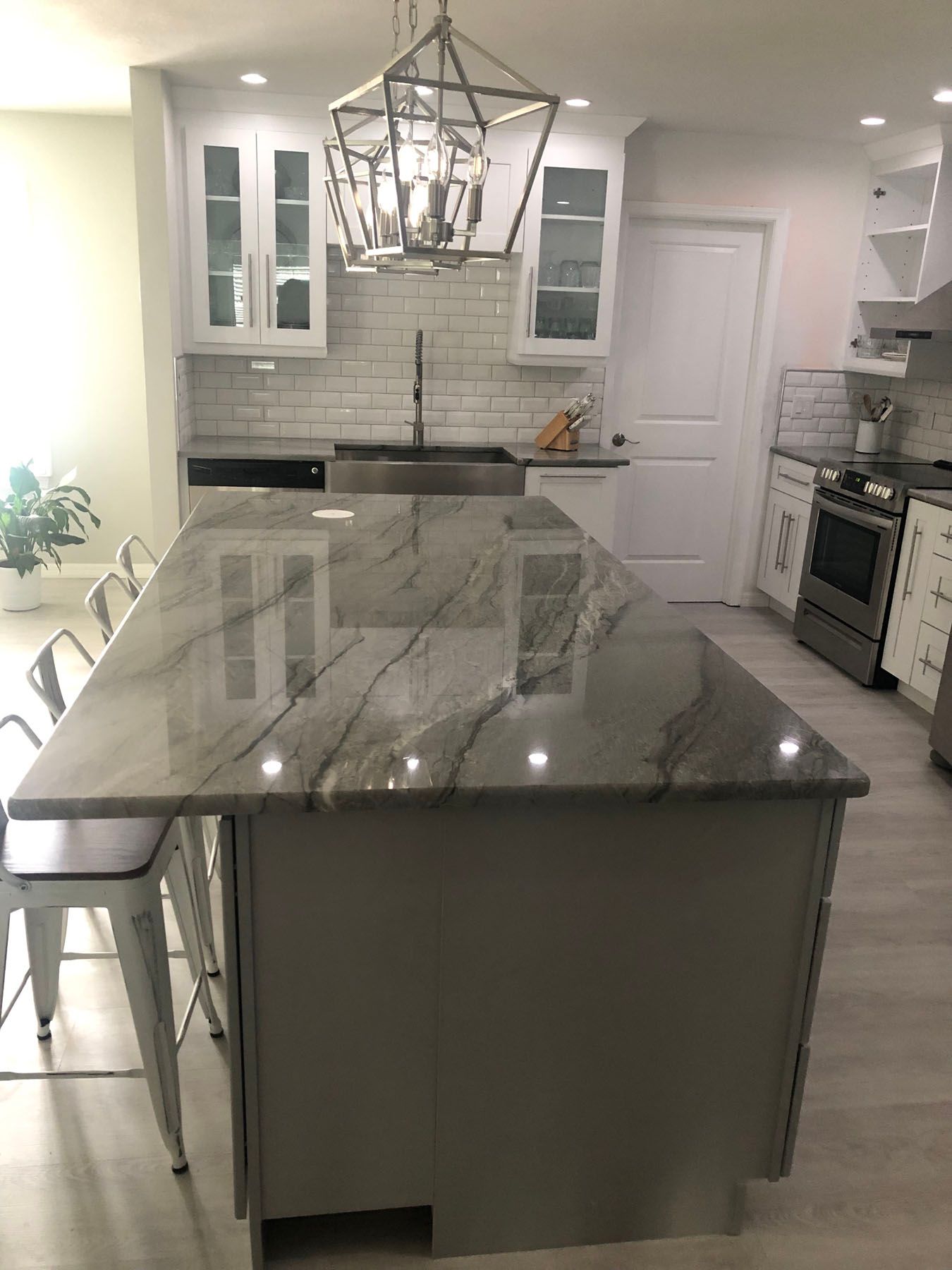 A modern kitchen island with a grey stone countertop and stools, positioned in front of a white sink and cabinetry.