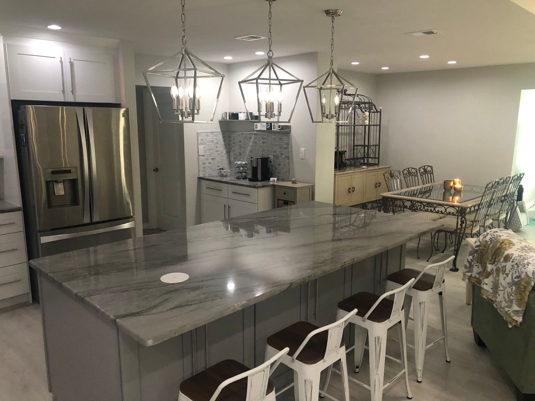 A modern kitchen featuring a gray island with white stools, three geometric pendant lights, and stainless appliances.