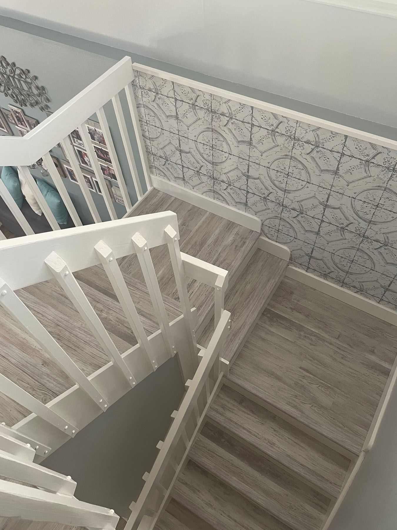 A high-angle view of a wooden staircase with white railings, beside a wall with gray and white patterned wallpaper.