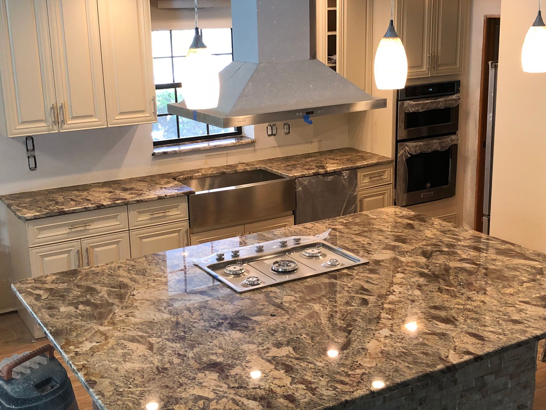A kitchen with white cabinets, speckled granite countertops, an island with a gas cooktop, and stainless steel appliances.