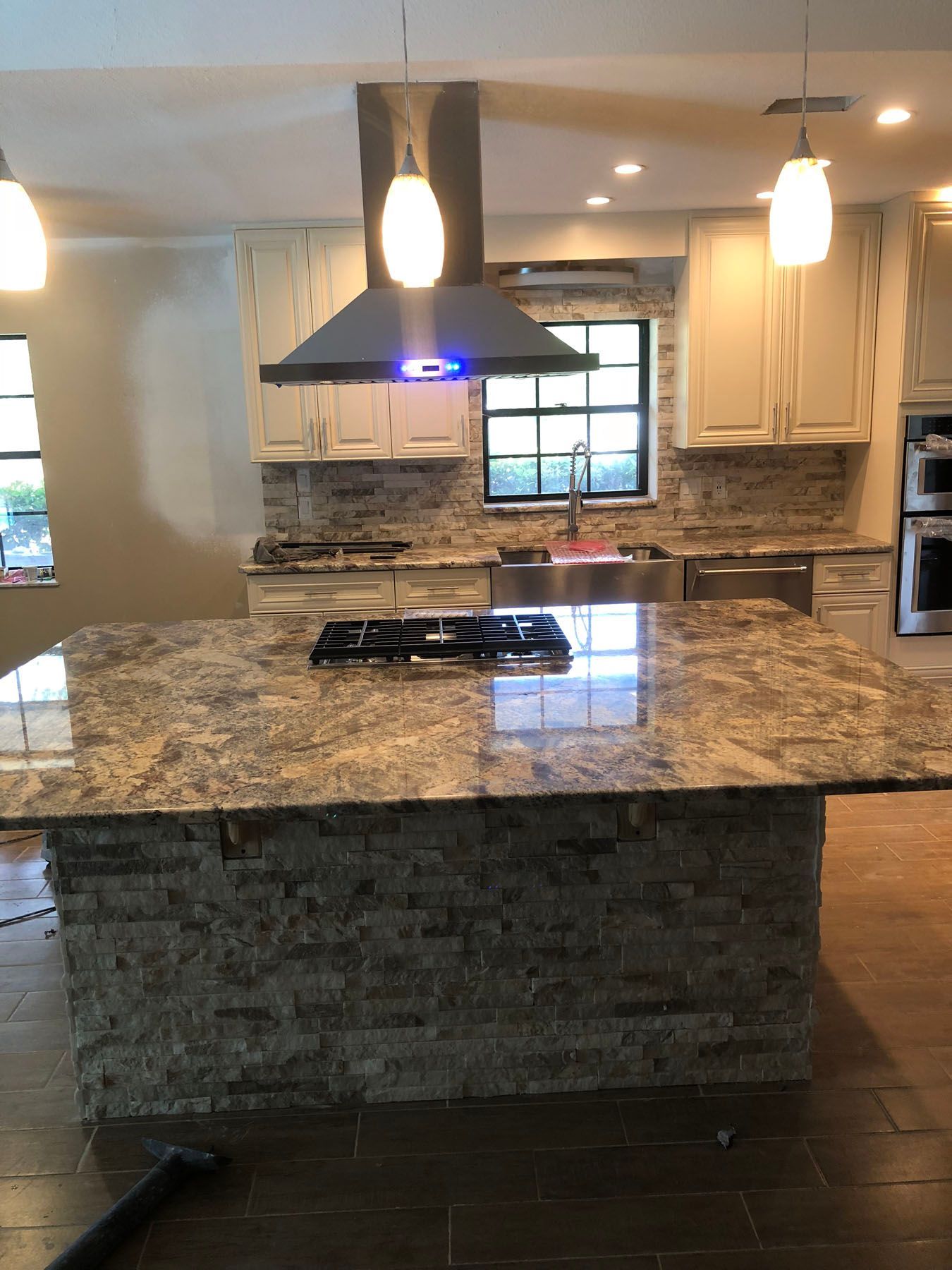 A kitchen island with a stone base and granite countertop, featuring a built-in cooktop, under pendant lighting.