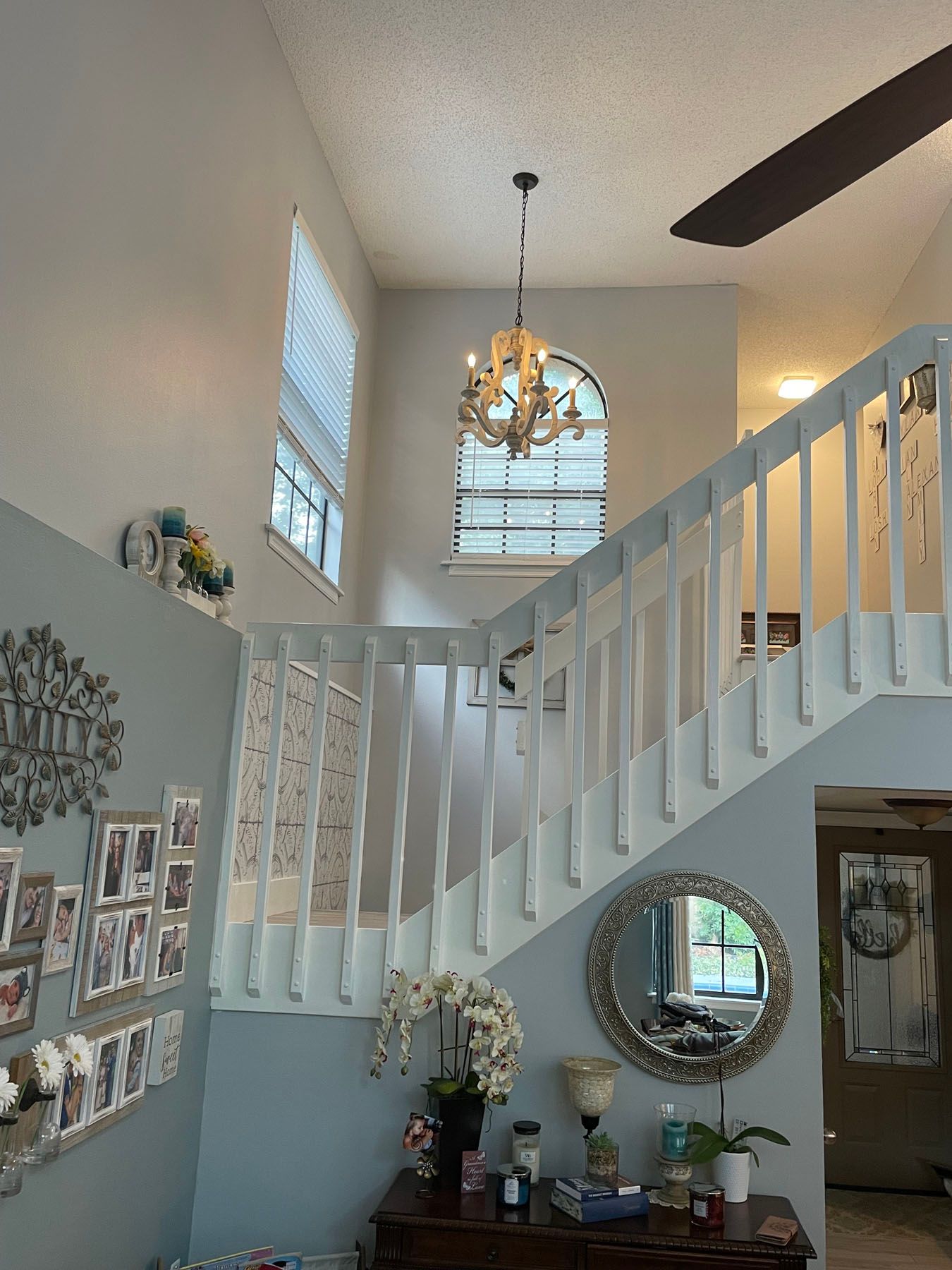 A bright foyer with a white staircase, a crystal chandelier hanging above, and a round wall mirror over a side table.