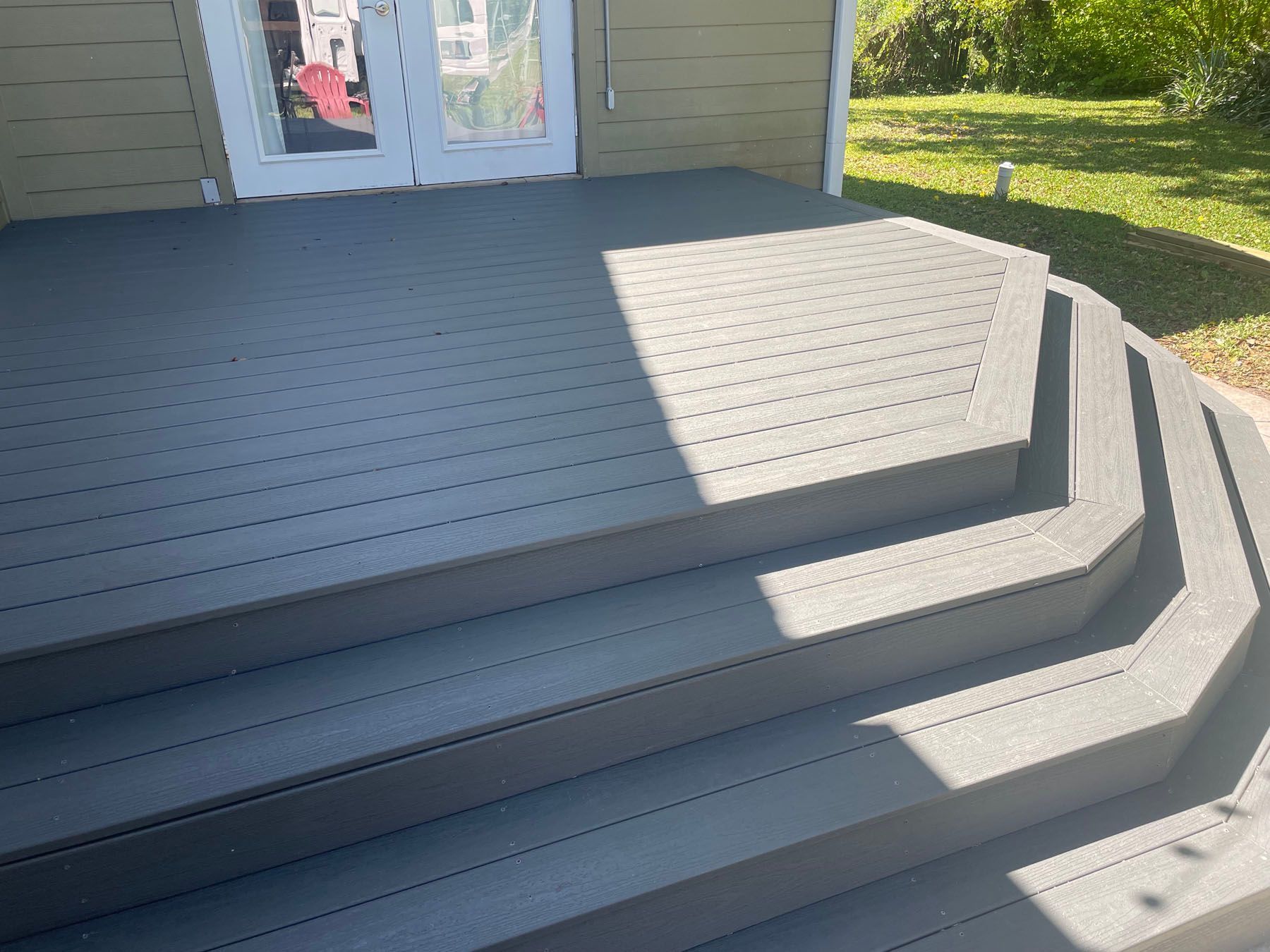 A grey composite deck with wrap-around steps leading to a set of double doors on the side of a house.