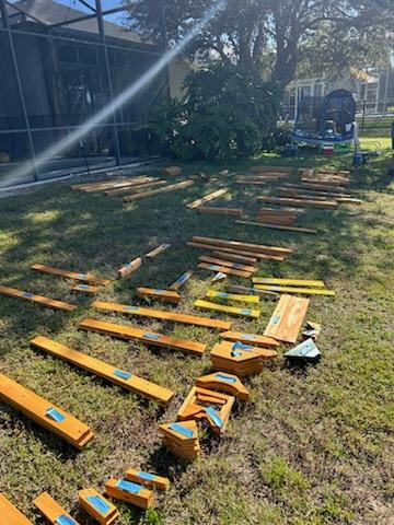 Wooden swing set parts and boards laid out in sections on a residential lawn for assembly.