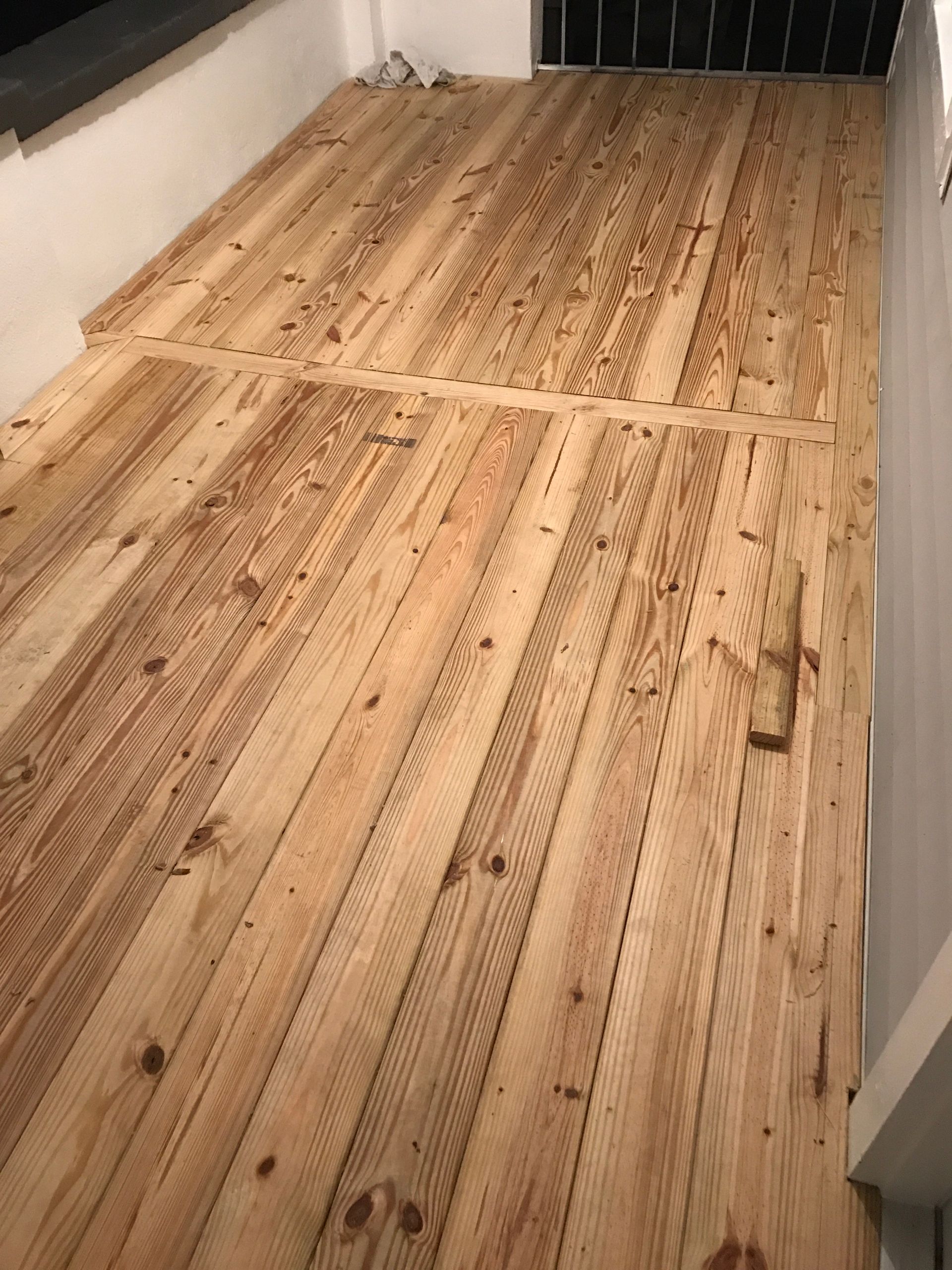 A wooden floor installation with light-colored planks running lengthwise, featuring a horizontal transition board.