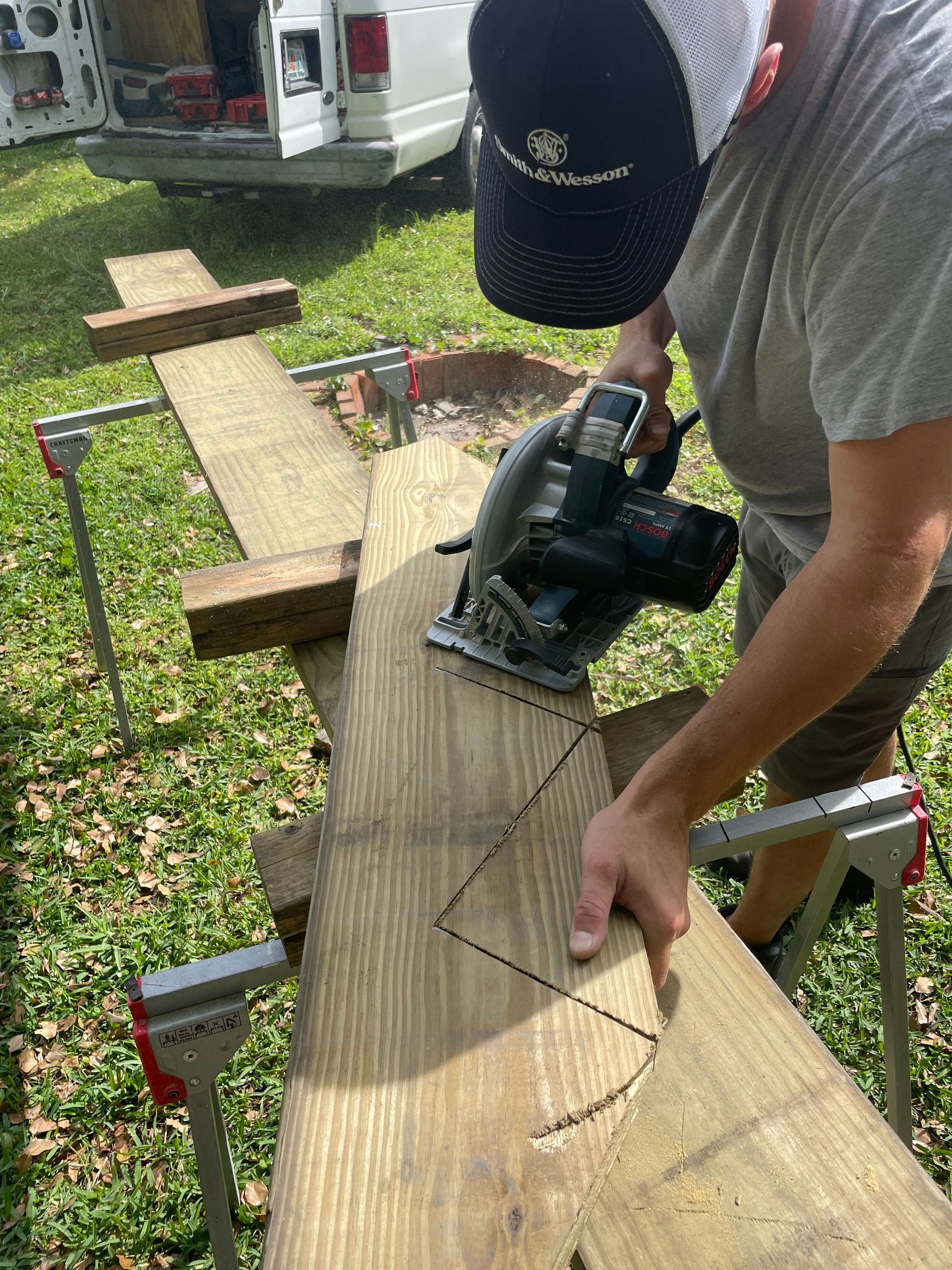 A person using a circular saw to cut a stair stringer pattern into a wooden board on sawhorses outdoors.