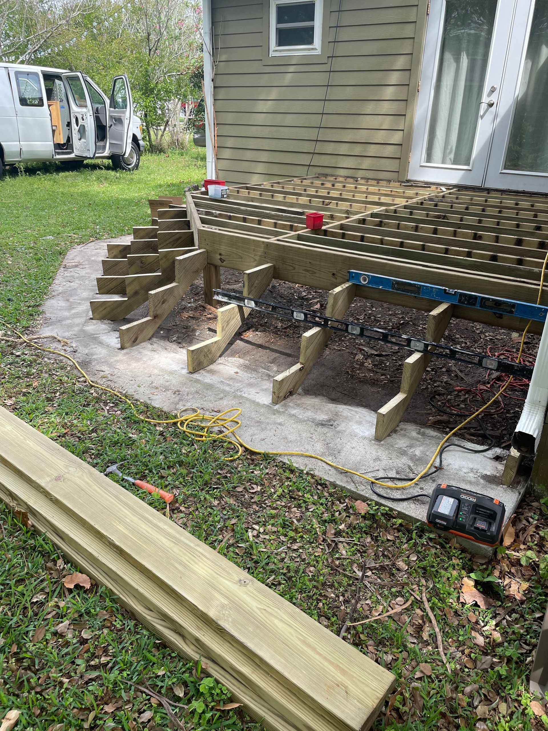 Construction project showing wooden staircase stringers installed on a concrete patio in front of a house.