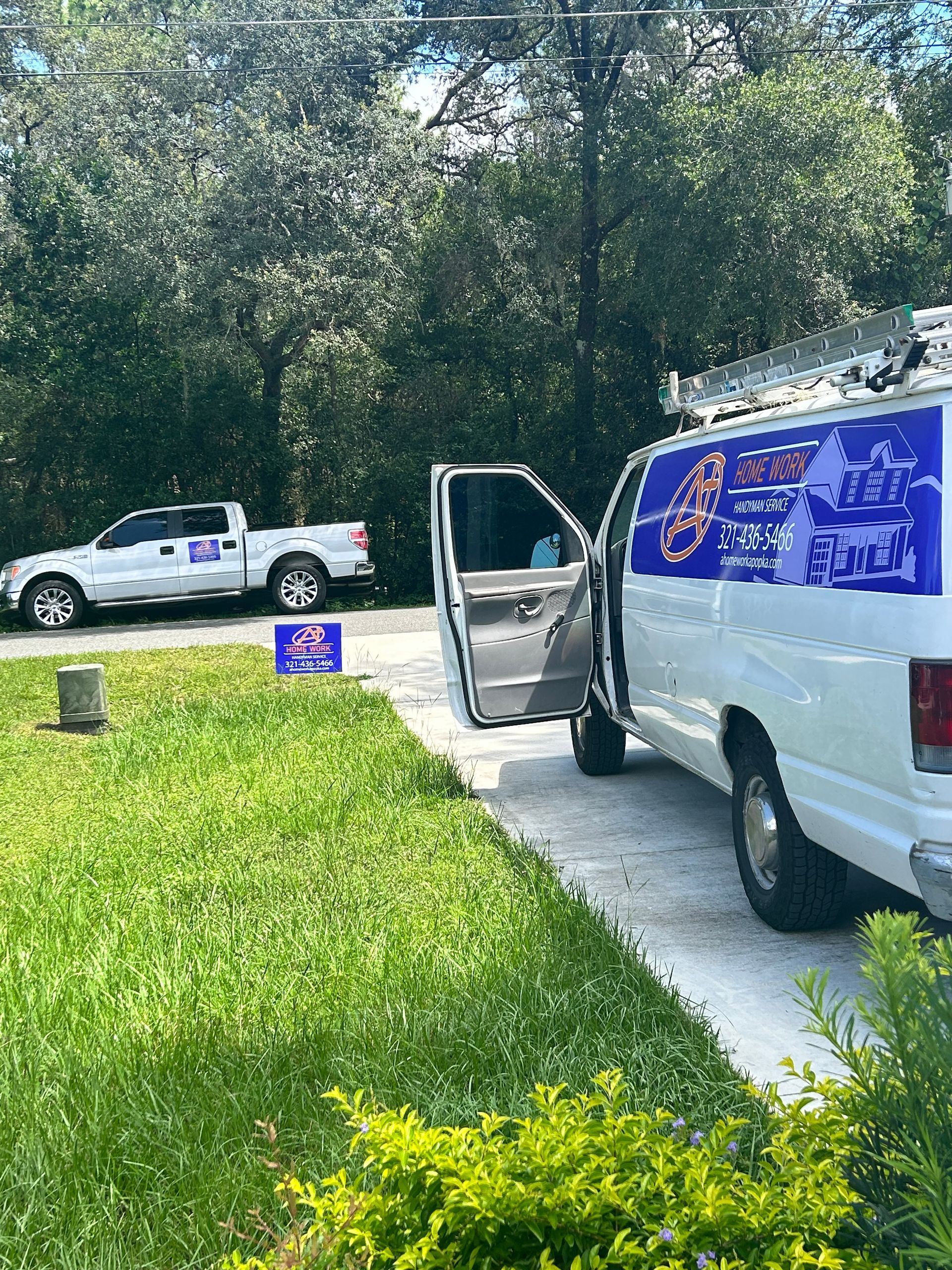 Two white service vans parked in a driveway near a grassy lawn with trees in the background.