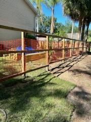 A newly constructed wooden fence with orange construction netting installed in a backyard next to a house.