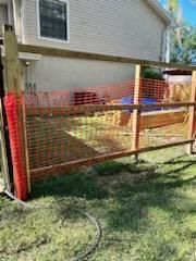 An unfinished wooden fence frame with orange plastic construction netting attached, standing in a residential yard.