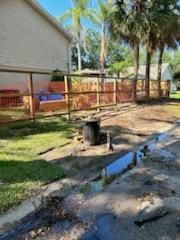 A wooden fence separates a residential yard from a concrete drainage ditch filled with standing water and debris.