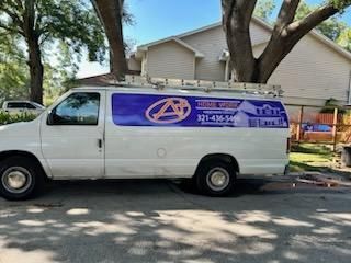 A white work van parked outdoors with a purple side decal featuring a logo, phone number, and building graphic.