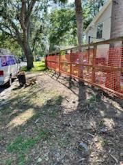 A bright orange construction safety fence installed along a wooden frame near trees, a house, and a parked white van.