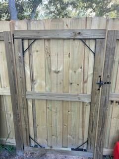 A wooden fence gate with a dark metal latch and four black corner-reinforcement brackets installed on the frame.