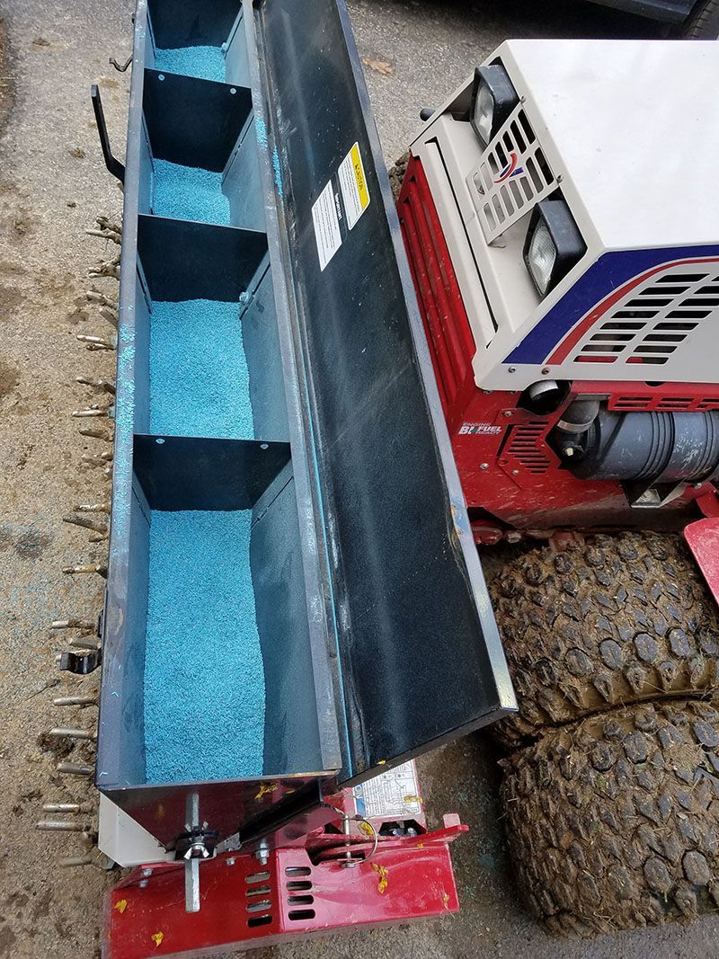 A red and white tractor with a conveyor belt filled with blue fertilizer