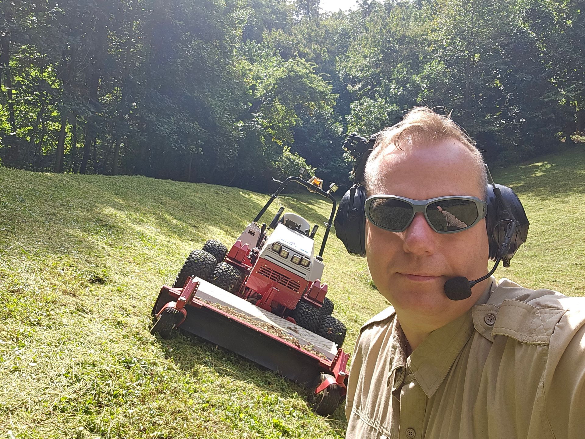 A man wearing headphones and sunglasses is standing next to a lawn mower.