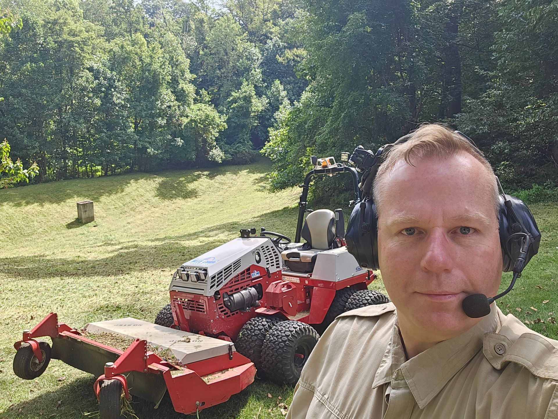 A man wearing headphones is standing in front of a lawn mower.