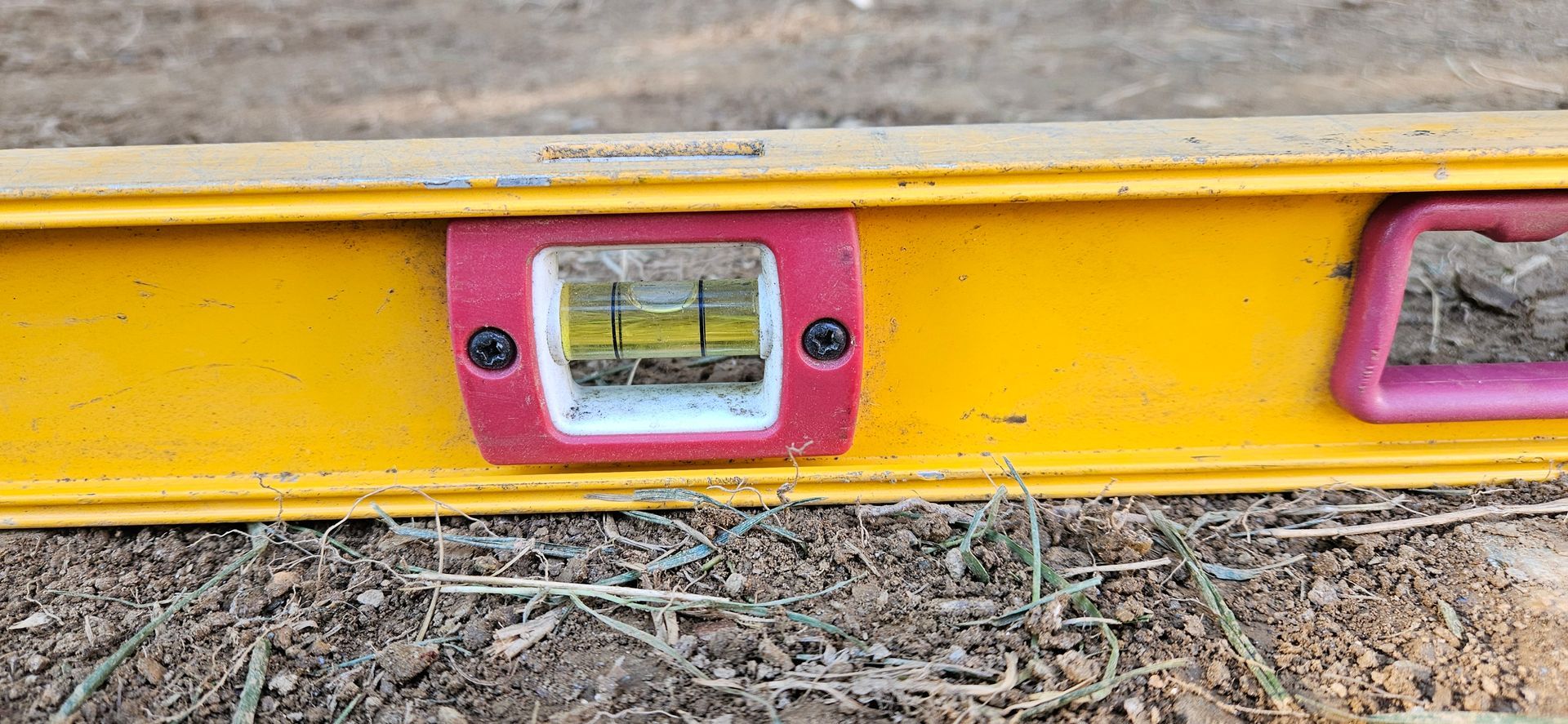 A yellow level is sitting on top of a pile of dirt.