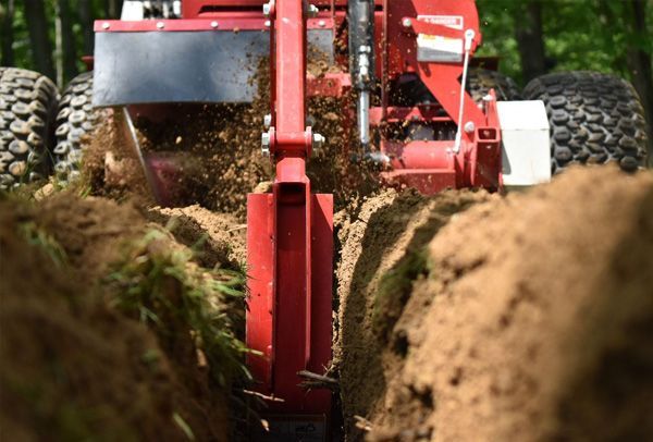 A red tractor is digging a trench in the dirt.