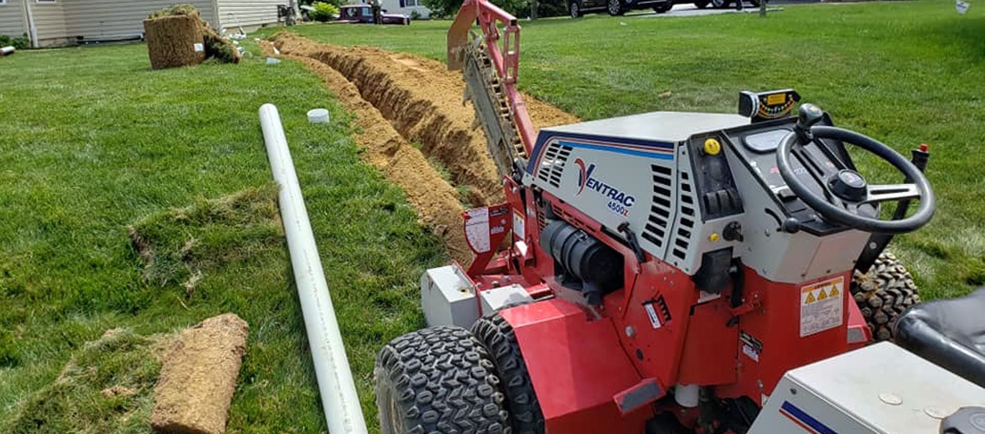 A red and white tractor is digging a hole in the grass.