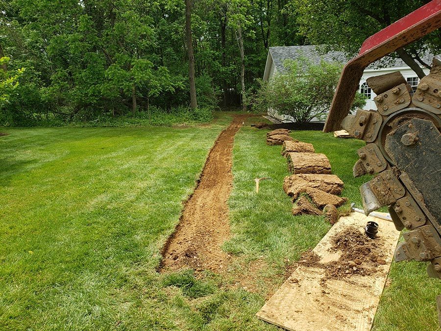 A tractor is digging a trench in the grass in a backyard.