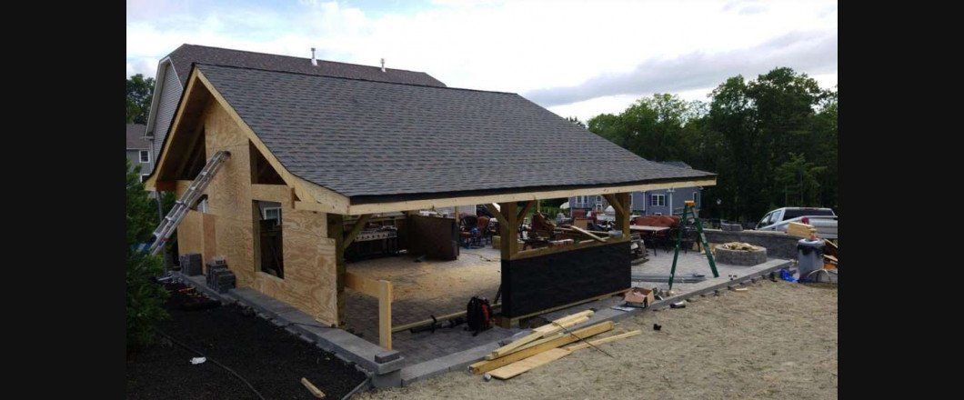 House under construction with exposed wooden walls and a dark roof in a muddy lot