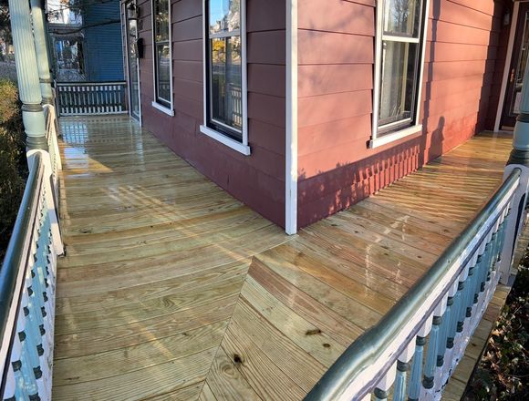 Wooden deck wrapping around a red house with white-trimmed windows and a metal railing.