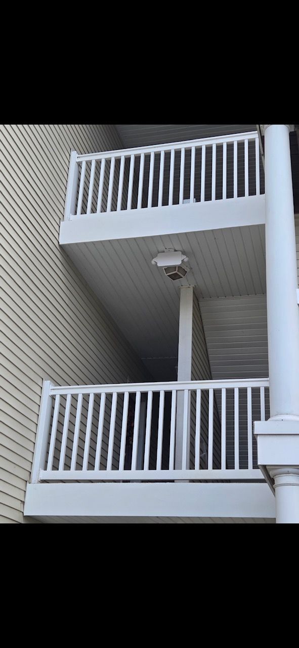 Two white balcony railings on a beige building, one above the other, with a mounted light between them